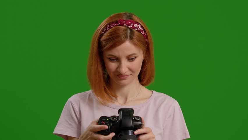 Happy female photographer searching through photos with green screen background. Successful shooting day for a proffesional.