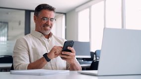 Close-up of middle aged Hispanic business manager ceo using cell phone mobile app, laptop. Smiling Latin or Indian mature man businessman holding smartphone sit in office working online on gadget. - Powered by Shutterstock - Get 15% off with code: PIKWIZARD15
