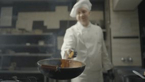 Male chef cooks dish on open fire. Man roasts food onhot frying pan on stove in kitchen. Slow motion