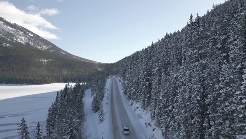 Aerial video flying over a car driving on the trails of Banff National Park in winter