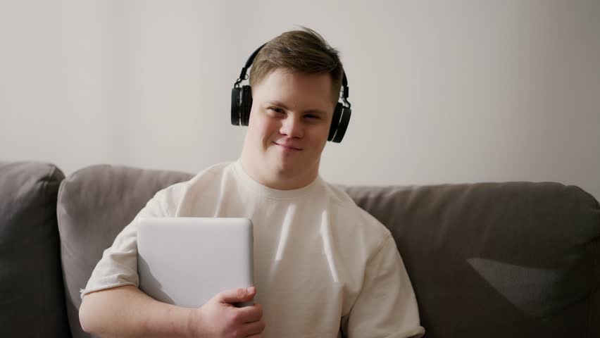 Man with down syndrome at home in headphones, holding laptop