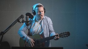 a man in a blue shirt plays the guitar and sings into a microphone. in the recording studio. slow motion video. High quality Full HD video recording