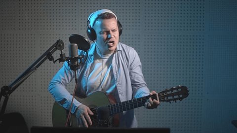 a man in a blue shirt plays the guitar and sings into a microphone. in the recording studio. slow motion video. High quality Full HD video recording Adlı Stok Video