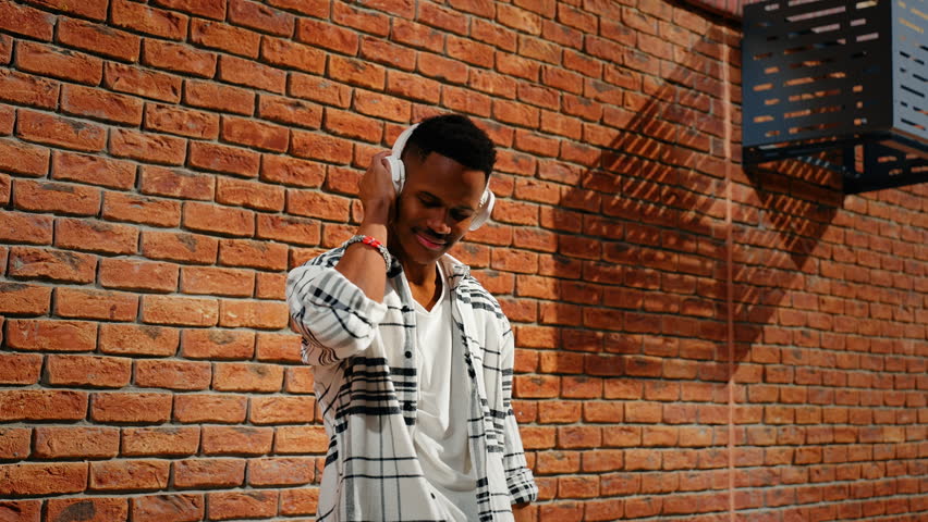  African American man walks down a city street in headphones and flips through music on a smartphone