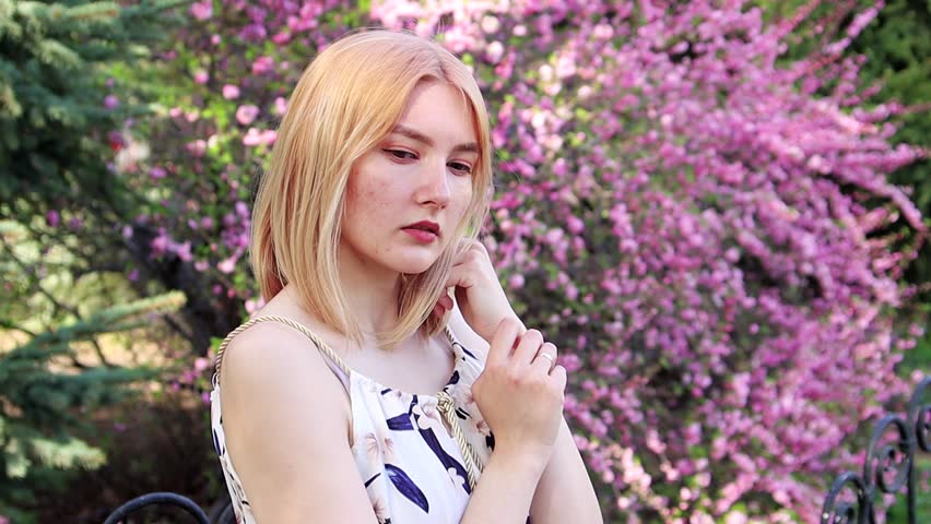 Portrait of a young woman dressed in a white dress, posing against the background of sakura, bokeh of pink flowers.