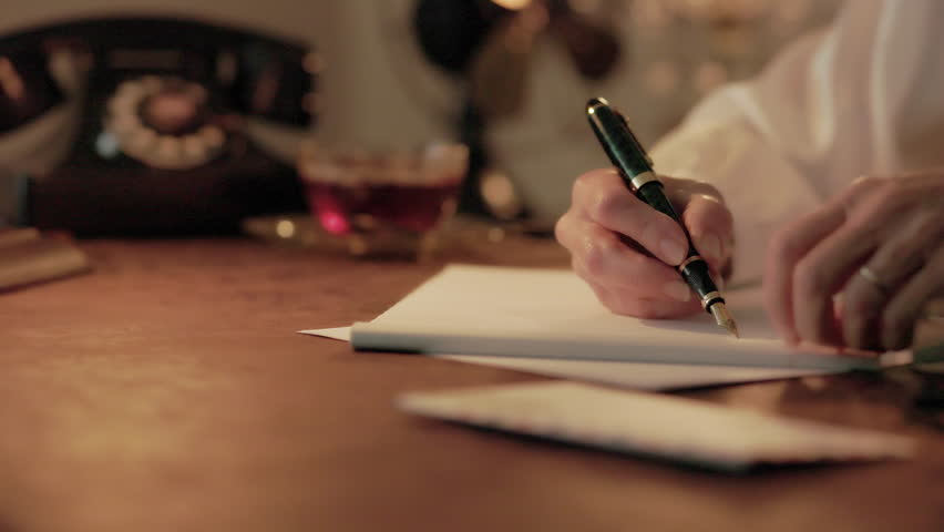 A scene from the 1930s or 1940s of a woman sitting at a desk writing a letter using a fountain pen. Royalty-Free Stock Footage #1104055937