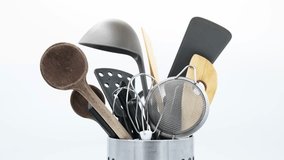 Kitchen utensils placed in a messy way in a metal container, rotate making a complete turn, isolated on white background. Strainer, scissors, ladle, wooden spoon, hand mixer. Real time video.