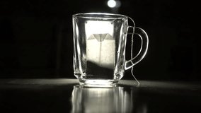 In a dark room, water is poured from a kettle into a transparent glass with tea bags inside