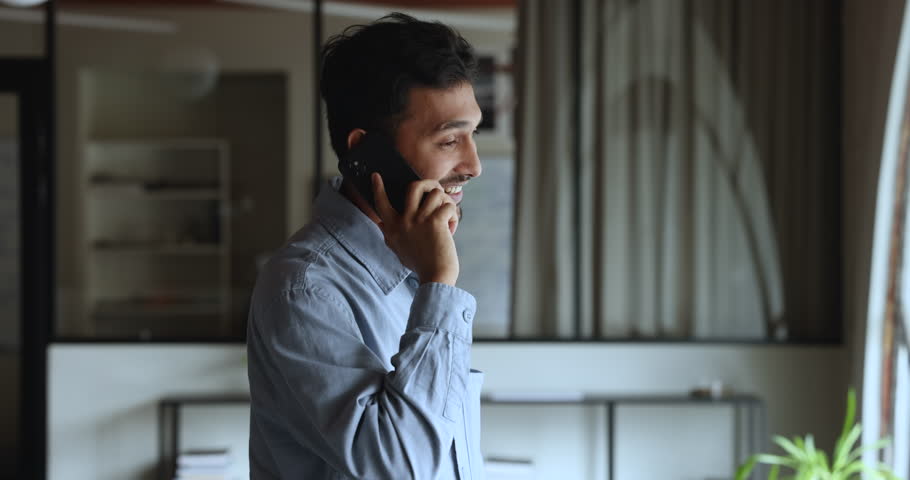 Successful Indian businessman lead conversation on cellphone stand in modern workplace, listen news, solves important issues with colleague, provide helpful information to client remotely. Phone call Royalty-Free Stock Footage #1104073269