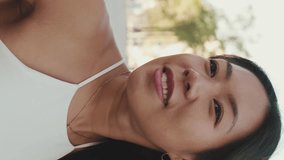 Vertical video, Close up, young woman is sitting on bench, looking away, turning her head and looking at the camera