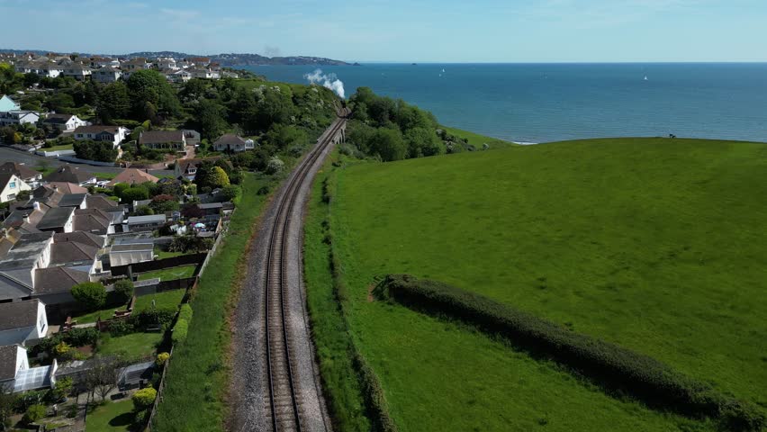 Broadsands, Torbay, Devon, England: DRONE AERIAL VIEWS: The drone flies towards a steam engine as the locomotive crosses a viaduct designed by the Victorian civil engineer, Isambard Kingdom Brunel. Royalty-Free Stock Footage #1104083153