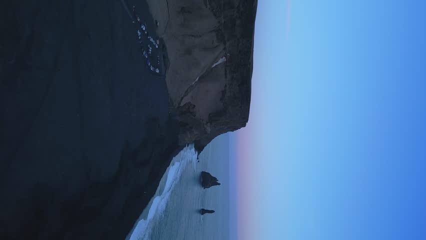 Vertical video: Aerial view of black sand beach with mountains and big stones in iceland, beautiful natural scenery on reynisfjara beach. Icelandic landscape with atlantic ocean on coastline. Slow