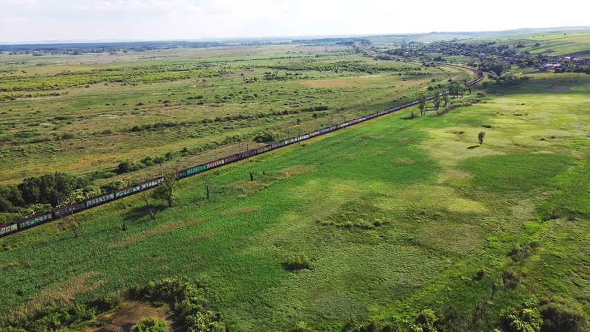 Freight-long trains carry with carriages a locomotive by the arid hilly landscape. Aerial drone perspective view at summer sunset. Royalty-Free Stock Footage #1104093247