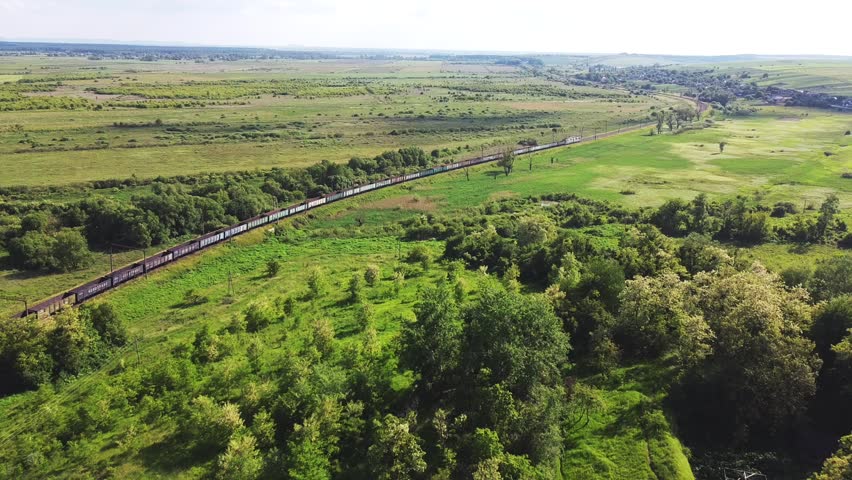 Freight-long trains carry with carriages a locomotive by the arid hilly landscape. Aerial drone perspective view at summer sunset. Royalty-Free Stock Footage #1104093257