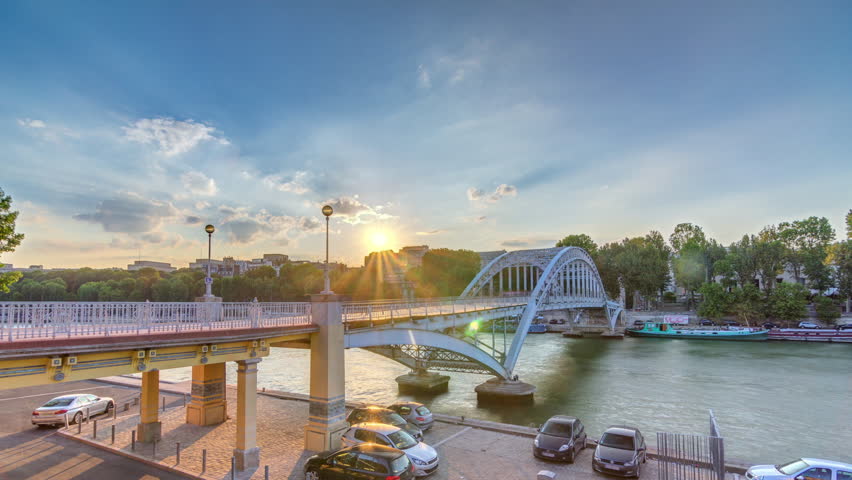 Passarelle Debilly footbridge during sunset timelapse with tourists observing the Seine river and the boats sailing on the water. Blue cloudy sky at summer day