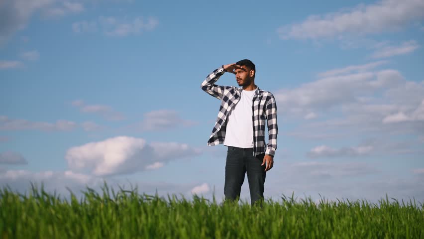 Standing and looking far away. Indian man in checkered shirt is on the agricultural field.
