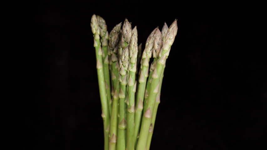 A bundle of asparagus spears rotates slowly on a black background and gradually disappears into darkness.