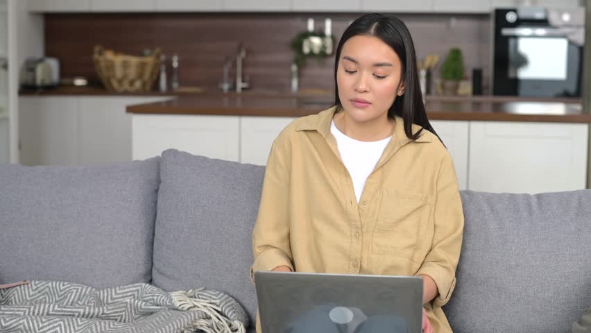 Young asian female businesswoman or female freelancer in comfy casual clothes sitting on the couch and working on the project, typing email on the laptop, writing an article Royalty-Free Stock Footage #1104100779