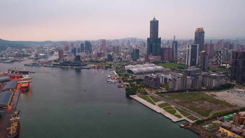  Aerial hyperlapse of Kaohsiung, a vibrant seaport city in Southern Taiwan, with 85 Sky Tower next to Exhibition Center by the harbor, Shoushan mountain in background and city lights glowing at dusk