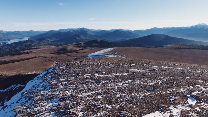 Aerial view, flying over volcano Bate Mahuida peak in Villa Pehuenia, Patagonia Argentina. View of the brown land, steep precipice and Andes mountains in the horizon, at sunset.