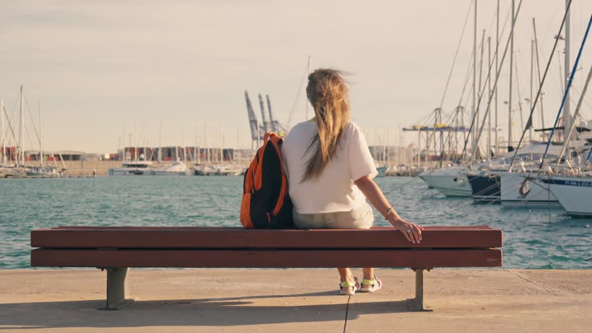 A tourist girl rests on a bench in a yacht club.