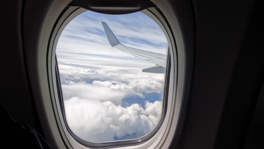Aircraft plane Wing of flying in clouds and blue sky airplane as seen by passenger through porthole windows. wide view 