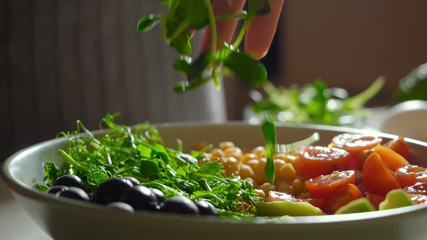 cooking healthy dinner concept, sunflower microgreens falling super slow motion. vibrant, healthy, colorful vegetarian bowl. vegetables, chickpeas , black olives, tomatoes, vegetable greens