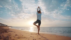 Barefooted woman doing yoga standing on one leg balancing in tree pose on sandy sea ocean beach at sunset. Female stretching relaxing concentrating on asana. Body care wellness sport activity concept. - Powered by Shutterstock - Get 15% off with code: PIKWIZARD15