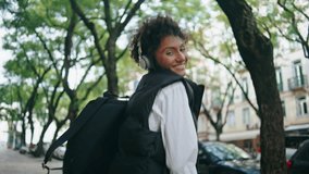 Joyful funky woman walking dancing along listening music in wireless headphones outdoors. Happy african american girl have fun enjoying sound in modern earphones. Smiling lady tourist strolling street - Powered by Shutterstock - Get 15% off with code: PIKWIZARD15