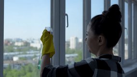 Woman cleaning window at home. Young woman housekeeper washing window glass with rag and spray detergent. Housework and housekeeping concept