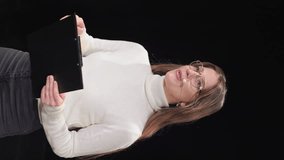 Confident caucasian woman in headset standing over black background and exchanging insights during mentoring. Motivational female speaker holding clipboard with notes for seminar.