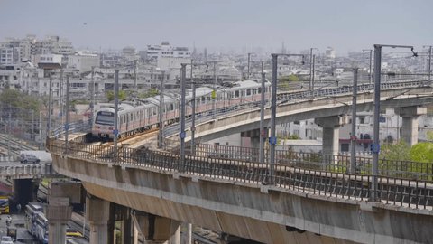 An elevated metro train is passing on a bridge on the subway track with the busy road with vehicles and urban Indian city landscape or buildings in the background, Jaipur, Rajasthan, India (May 2023) Redaksjonell arkivvideo