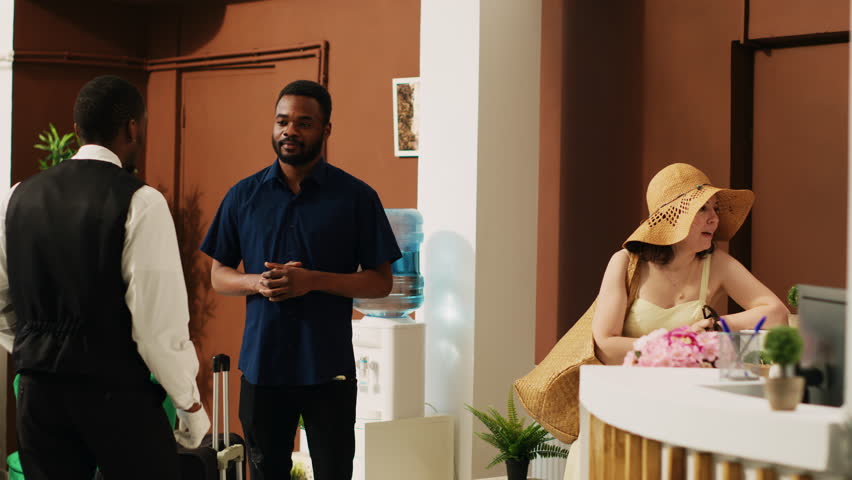 Peole giving cash to bellhop in lobby, employee providing luxury service and carrying luggage trolley bags. Hotel guests paying money tip to bellboy in resort lounge area, vacation trip.