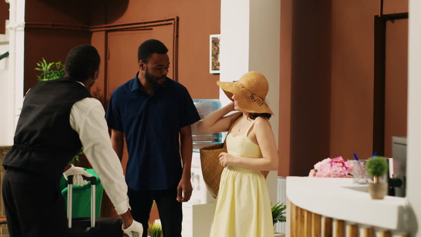 Peole giving cash to bellhop in lobby, employee providing luxury service and carrying luggage trolley bags. Hotel guests paying money tip to bellboy in resort lounge area, vacation trip.