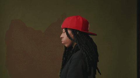Side shot of non binary person wearing red cap against studio backdrop วิดีโอสต็อก