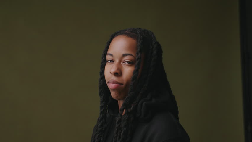 Non binary person with braids looking at camera ageist studio backdrop