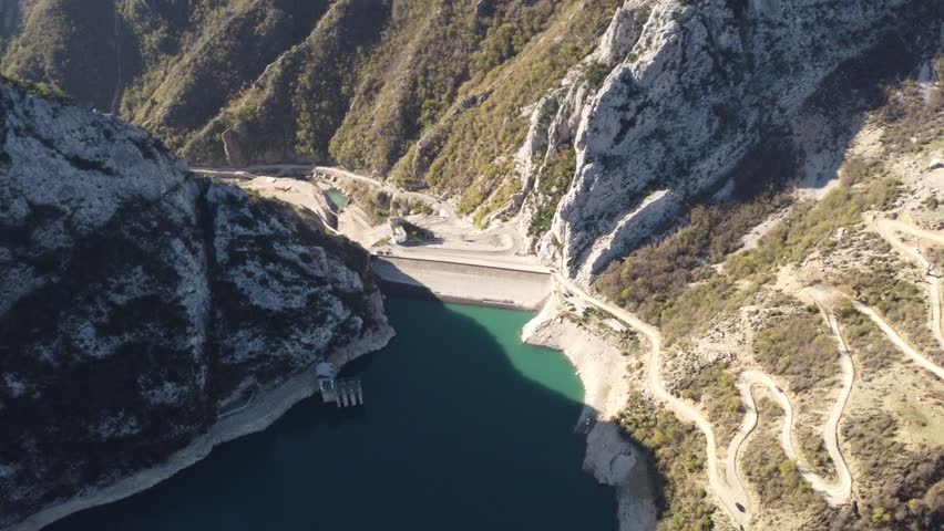 Aerial view of steep serpentine road in the mountains near the reservoir. Winding dirt road. Bovilla Lake Albania. Drone video.