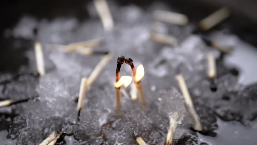 Couple of Matches Burn in a Passionate Kiss on Background of Falling Wet Snow. Dramatic love story two dying matchsticks in a bright fire. Lots of frozen matches on ice. Death, attack, war, Ukraine.