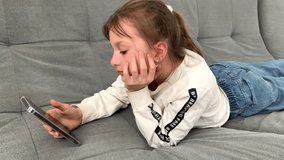 a child plays on a mobile phone, sitting on the couch at home, a girl communicates, watches videos on a mobile phone, cyberspace, entertainment for modern children.