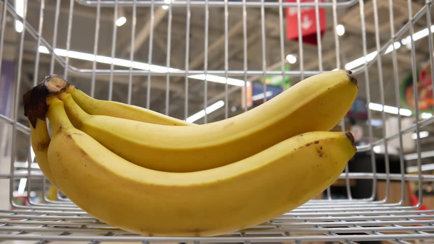 A buyer puts a bunch of ripe bananas in a shopping cart close-up Royalty-Free Stock Footage #1104157357