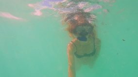 A pregnant woman explores the underwater world while snorkeling in the vibrant blue sea. With a dive mask and breathing tube, she records her exhilarating journey using an action camera, preserving