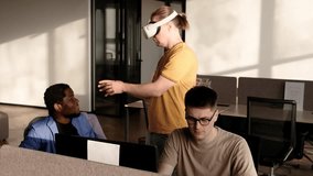 IT Development Team Working on VR Project. Man wearing VR headset, playing and touching something in the virtual world. Diverse men programmers using VR technologies and computer to create video game. - Powered by Shutterstock - Get 15% off with code: PIKWIZARD15