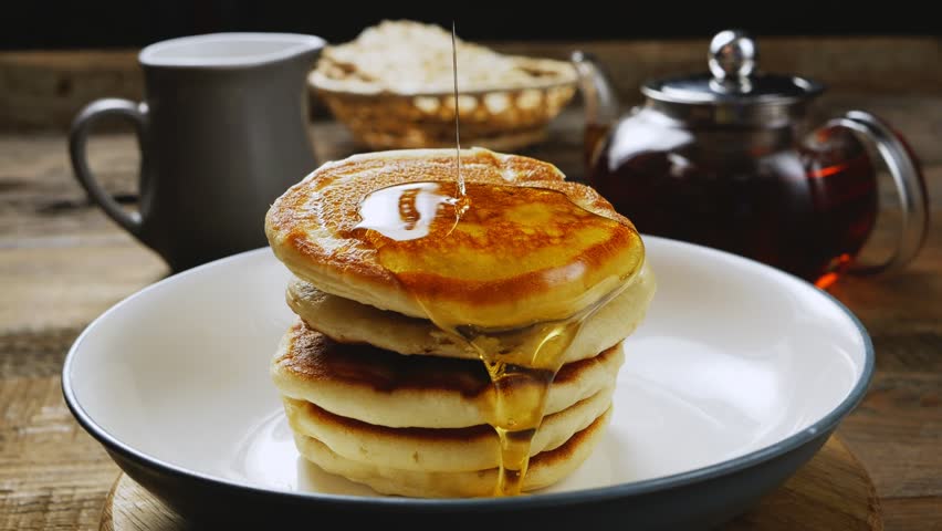 Homemade pancakes in a gray plate are poured with a thin stream of slow motion honey. Medium plan. Royalty-Free Stock Footage #1104163521