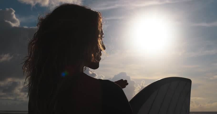 Silhouette profile of surfer woman looking at epic view golden hour, back rear view, female surfer concentrating and mind setting for training workout, thinking about upcoming surfing session training