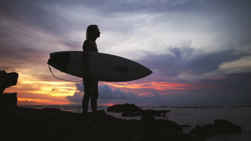 Silhouette of male surfer traveler tourist at dramatic epic sunset. Man calmly motionless contemplates serene surface of sea water. Admiration, enthusiastic contemplation of amazing places on vacation Royalty-Free Stock Footage #1104165485