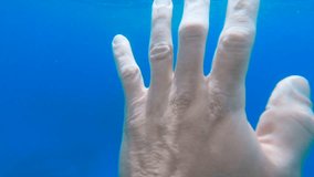 Underwater view of a caucasian adult left hand swaying in the sea in slow-motion.