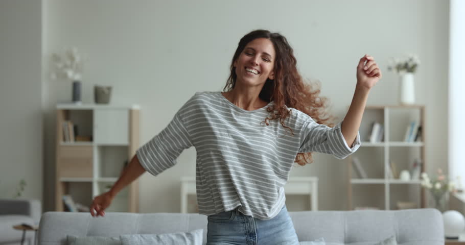 Happy young single lady having fun, dancing in cozy living room. Millennial Hispanic woman fooling, moving to favourite, cool music feels untroubled on weekend leisure at modern home. Active pastime Royalty-Free Stock Footage #1104169441