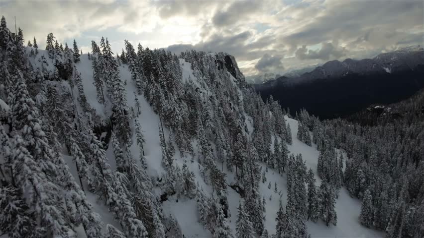 Canadian Rocky Mountain Landscape covered in snow in British Columbia, Canada. Cloudy Sunset Sky. Aerial Flight
