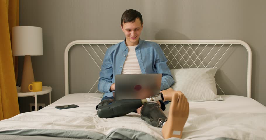 Happy freelancer caucasian man with artificial bionic legs prosthesis remote working at home on his laptop computer, cheerful guy using laptop, technology, businessman working online job profession | Shutterstock HD Video #1104175673