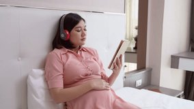 Pregnant woman relaxing by listening to music on headphones via bluetooth from tablet and, healthy pregnancy health concept. - Powered by Shutterstock - Get 15% off with code: PIKWIZARD15